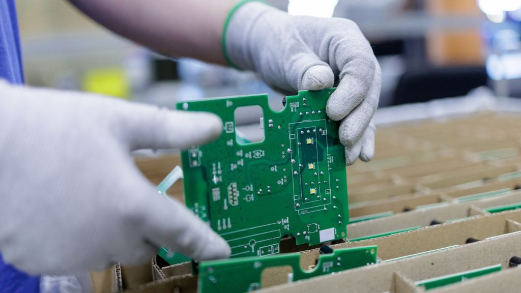Technician inspecting a green printed circuit board before deciding repair or remake